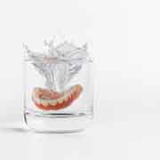 Dentures splashing into a clear glass of transparent fluid with a white background